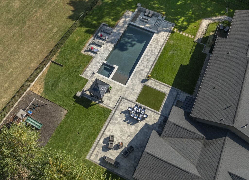 Aerial view of a luxurious backyard featuring a modern swimming pool, stylish patio furniture, a gazebo, and landscaped lawn, showcasing a custom pool design by Tango Pools.