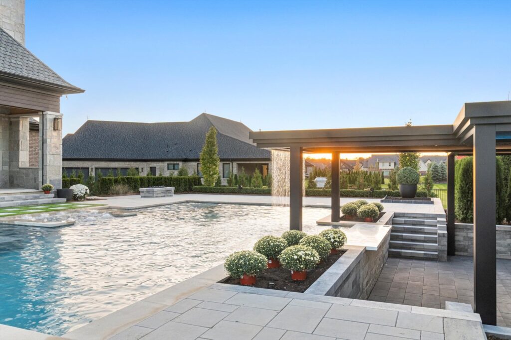 Luxury pool area featuring a sparkling blue pool, elegant landscaping, and modern outdoor structures, showcasing a serene backyard retreat designed by Tango Pools in Macomb.
