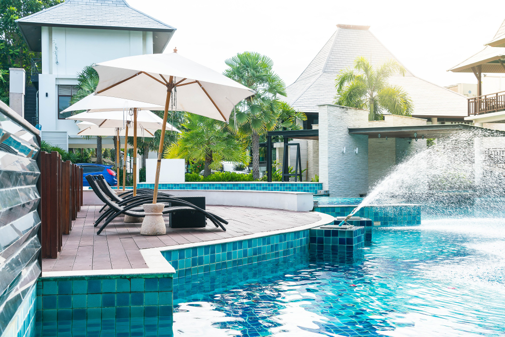 Luxury swimming pool with sun loungers and umbrellas, surrounded by tropical landscaping and modern architecture, showcasing a tranquil outdoor oasis by Tango Pools.