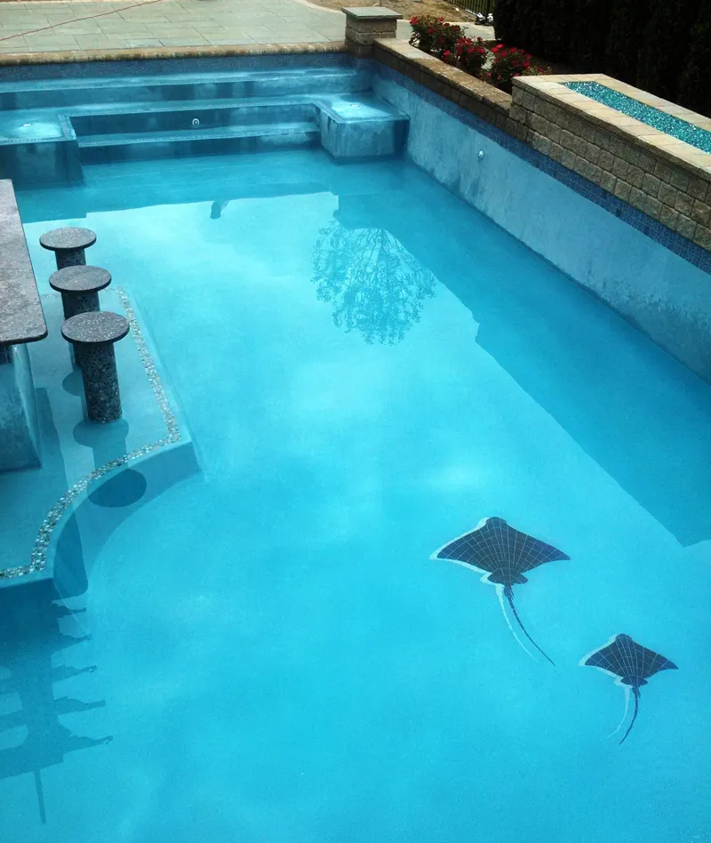 Luxury pool with polished plaster finish, featuring decorative stingray designs on the bottom, surrounded by a sleek bar area and natural stone accents, showcasing a contemporary aesthetic ideal for Michigan homeowners.